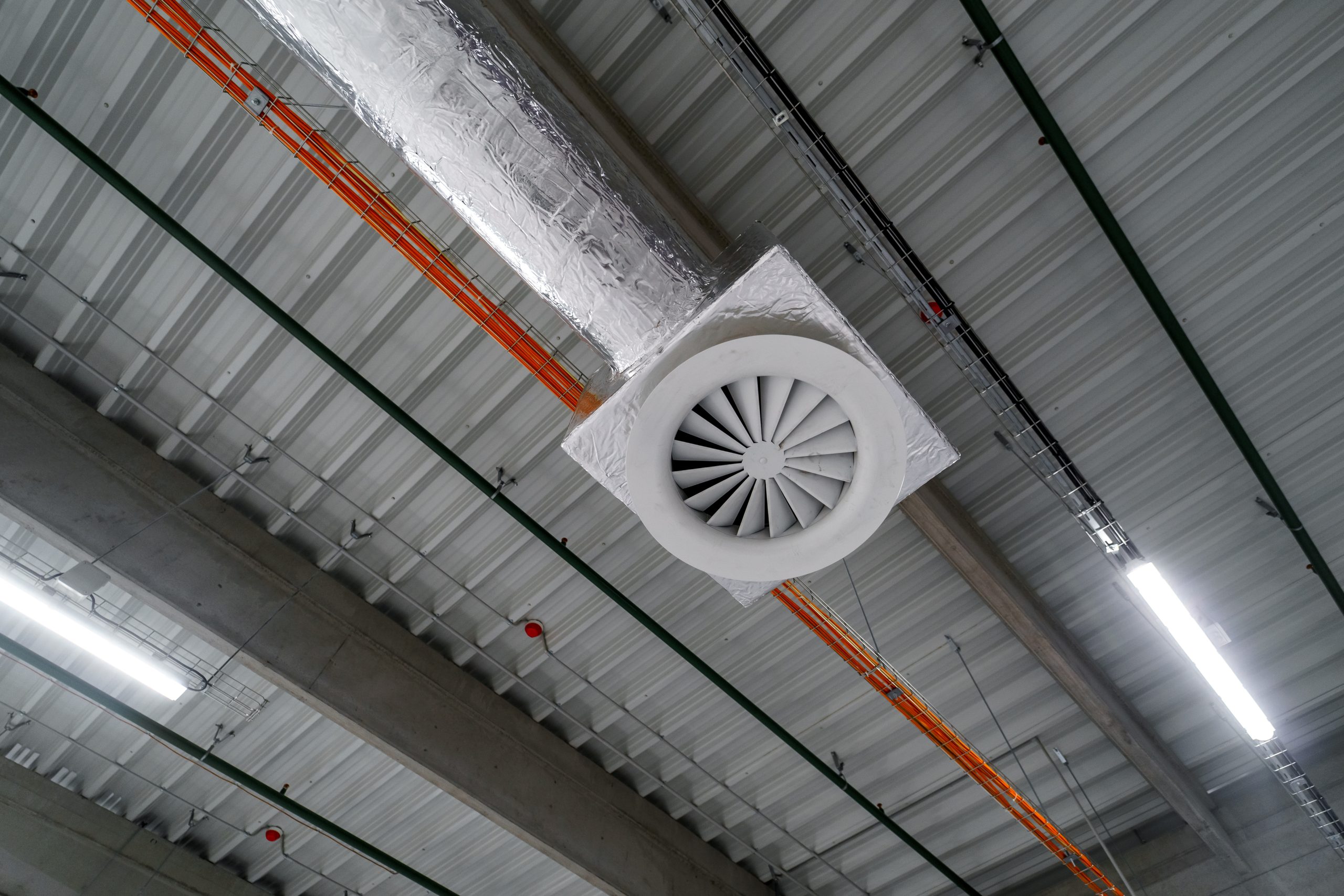 Air ventilation system on the ceiling in a large warehouse. Pipes made of silver insulating material hang from the ceiling inside the new building