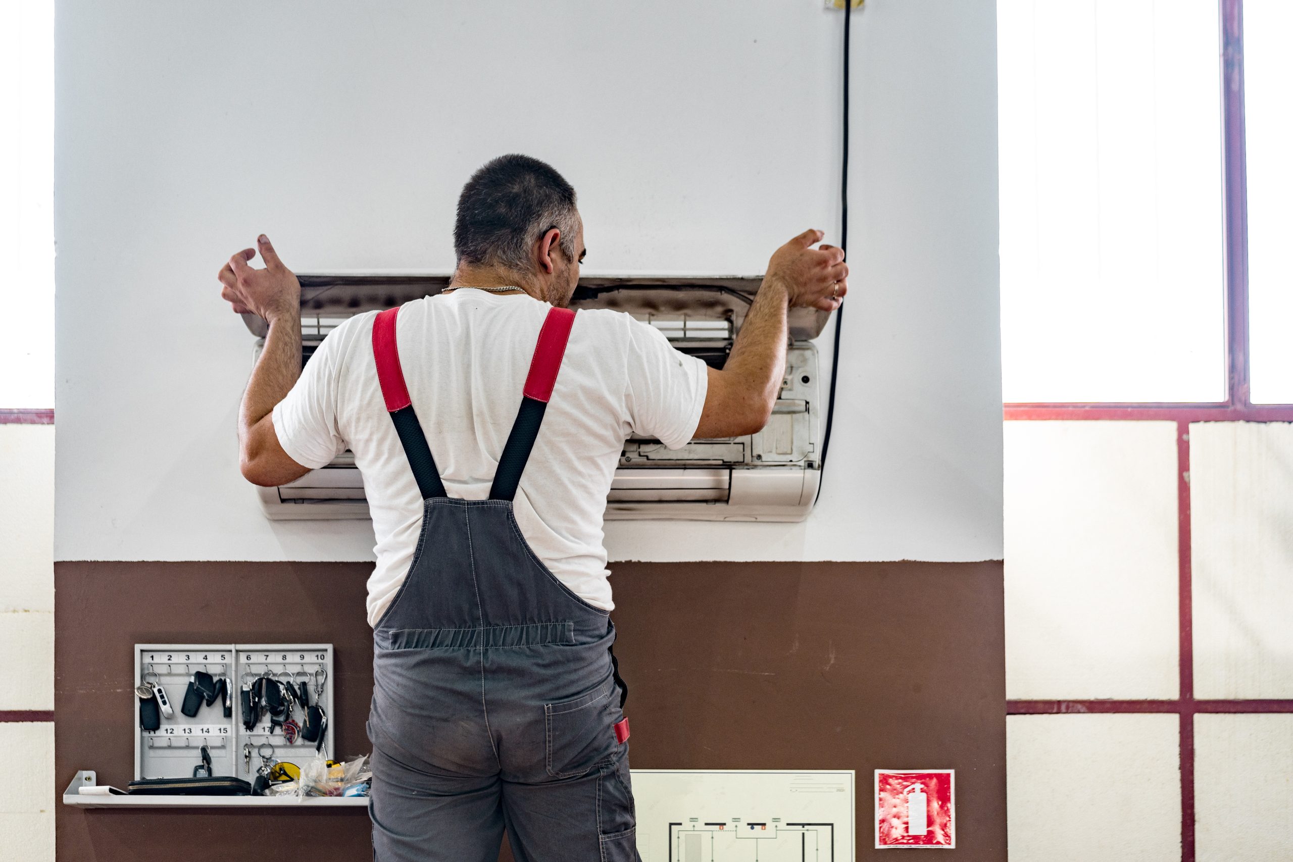 Repairman checking and repairing air conditioner indoors, back view