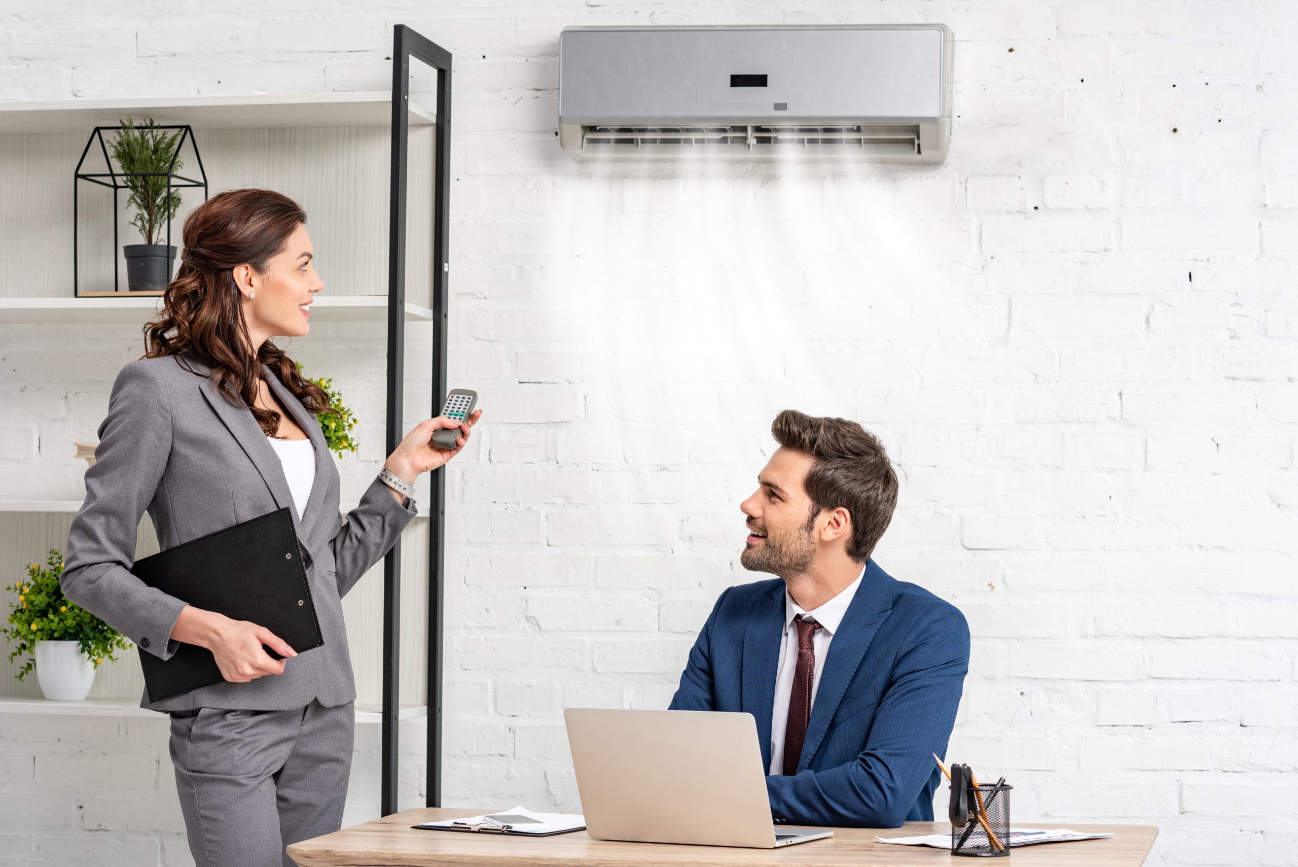 smiling businesswoman holding remote control while standing near handsome manager sitting at